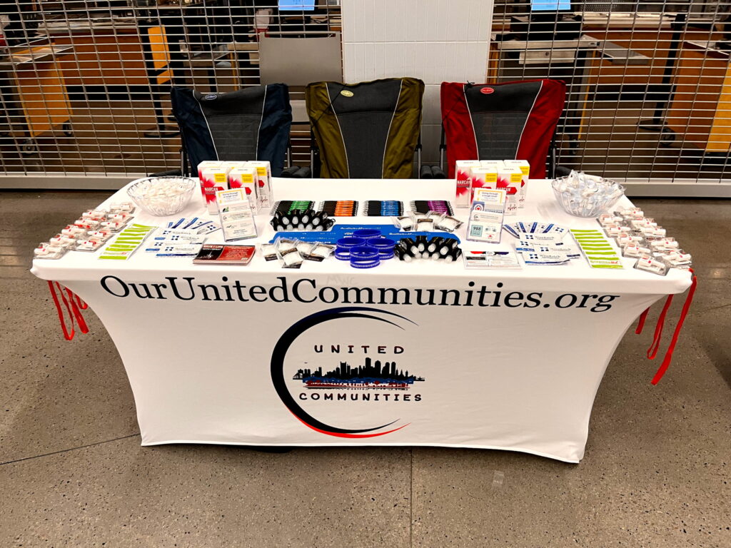 Outreach table for United Communities Corp. with a white branded tablecloth, informational flyers, and Narcan kits neatly displayed at the Weymouth Health Fair community event.